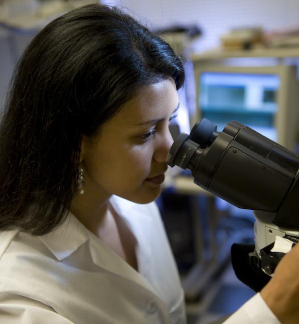 Woman in a lab coat looking through a microscope